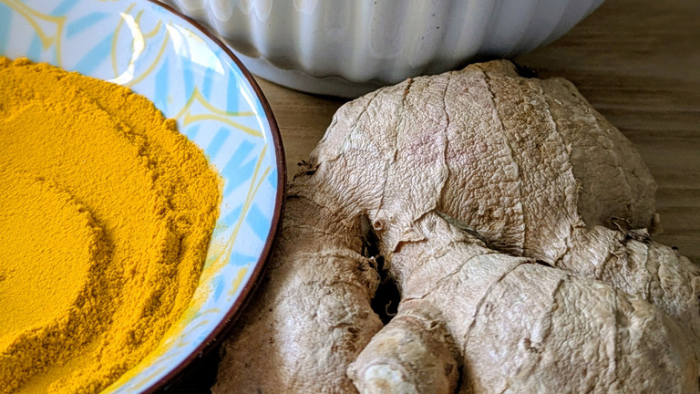 Ingwerwurzel neben Schälchen mit Kurkuma Ingwerwurzel neben Schälchen mit Kurkuma