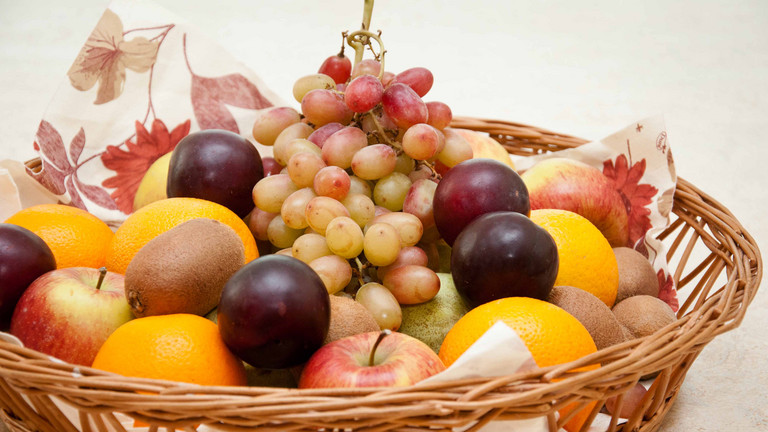 Ein Korb mit verschiedenem Obst wie Weintrauben, Äpfeln und Orangen