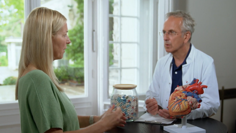 Prof. Dr. Michalsen und eine Patientin stehen an einem Tisch mit einem Herzmodell und unterhalten sich, Long-Covid, Corona, Herzmuskelentzündung, NDR Natur-Docs, TV-Tipp, Immanuel Krankenhaus Berlin, Berlin-Wannsee Prof. Dr. Michalsen und eine Patientin stehen an einem Tisch mit einem Herzmodell und unterhalten sich