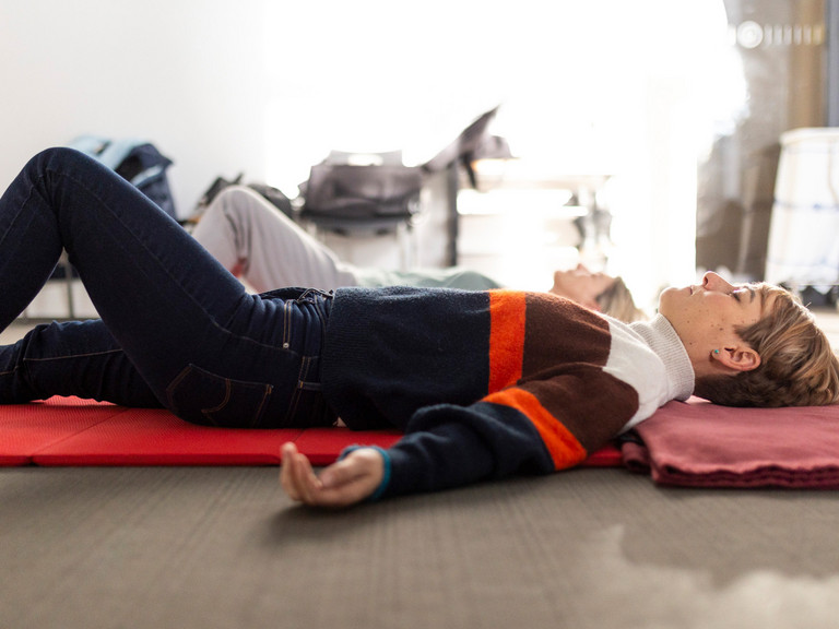 Frauen liegen mit geschlossenen Augen auf Matte und praktizieren achtsames Yoga