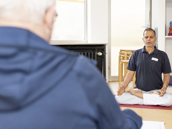 Therapeuth sitzt im Schneidersitz und leitet Atemübungen an